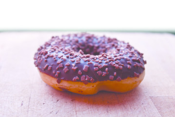 Chocolate donut with sprinkles isolated on wooden background.