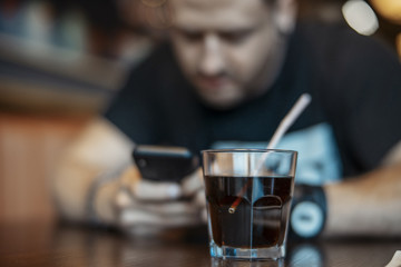 Young attractive man looking at mobile phone screen and drinking soda.