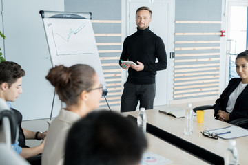 Confident businessman standing near the whiteboard and performing for his colleagues at boardroom