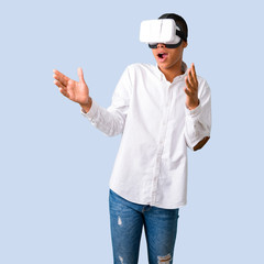 Young african american man with white shirt using VR glasses. Virtual reality experience on isolated blue background