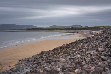 Ballinskellig Bay in Waterville - beach with red stones against dramatic sky, Ireland
