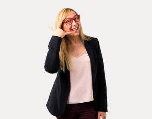 Middle-age blonde business woman with black jacket making phone gesture and speaking with someone. Call me back sign on isolated grey background