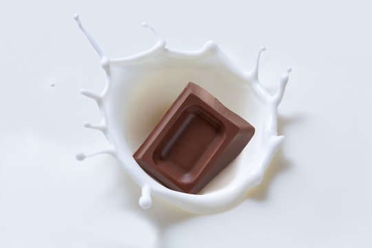 A piece of chocolate falling into the milk with a splash in the form of a crown