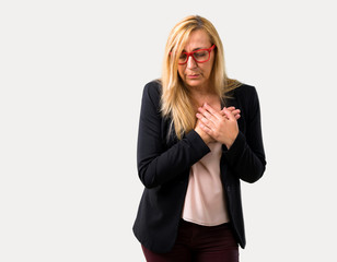 Middle-age blonde business woman with black jacket having a pain in the heart. Heart attack on isolated grey background