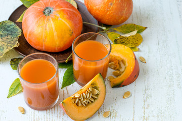 Two glasses with natural homemade juice and a fresh ripe pumpkin on an old wooden table. The concept of healthy eating.