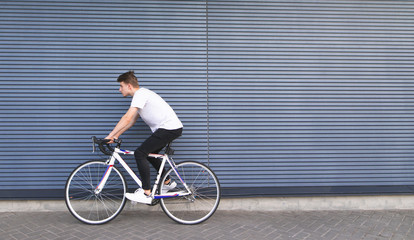 Young man in a white T-shirt rides on a white highway on the background of the wall. Portrait of a...