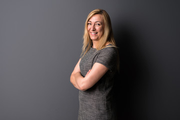 Middle age blonde woman on grey background keeping the arms crossed while smiling