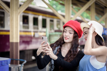 Asian women traveler have playing a mobile phone and talking for waiting the train with happiness at Hua Lamphong station at Bangkok, Thailand.