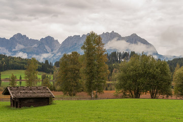 Kitzbühel, Schwarzsee und Wilder Kaiser im Herbst mit Hochnebel, Wolken, grüner Wiese und Bauernhütte