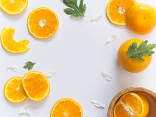 Sliced oranges on white background decorated with white and green leaves and a orange in wooden bowl on corners
