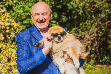 Senior man with his pet little red pekingese dog at home yard. American mature man with a dog....