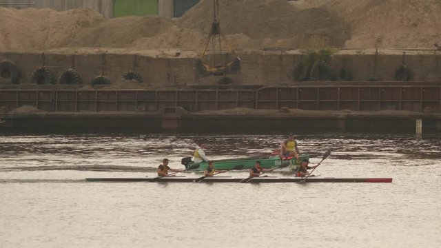 Four oarsmen swim in a kayak and next to the boat sails the coach, outdoor