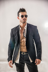 Elegant muscular attractive young man with white shirt open on naked torso, against white wall