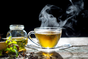 Hot tea in glass teapot and cup with steam on wood background
