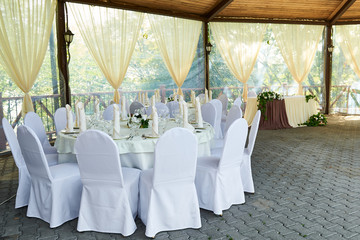 Wedding. Banquet. The chairs and roundtable for guests served with cutlery, flowers, and crockery and covered with a tablecloth