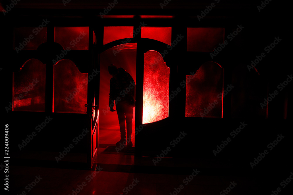 Wall mural Silhouette of an unknown shadow figure on a door through a closed glass door. The silhouette of a human in front of a window at night. Scary scene halloween concept of blurred silhouette