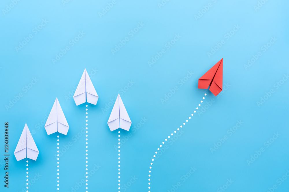 Wall mural group of white paper planes in one direction and one red paper plane pointing in different way on bl