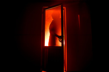 Fototapeta premium Silhouette of an unknown shadow figure on a door through a closed glass door. The silhouette of a human in front of a window at night. Scary scene halloween concept