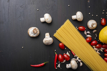 Spaghetti ingredients on black wooden desk, top view.