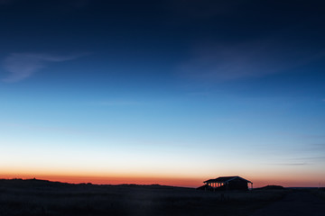 Landscape midnight sunset view with a house at the sand dunes overlooking the sea and colorful gradient sky.  Lønstrup in North Jutland in Denmark, Skagerrak, North Sea