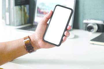 Cropped shot a man's hand holding blank screen mobile phone on desk.