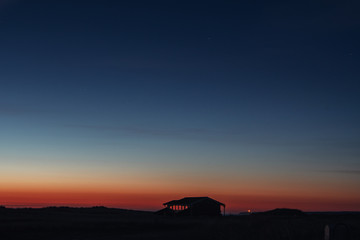 Landscape midnight sunset view with a house at the sand dunes overlooking the sea and colorful...