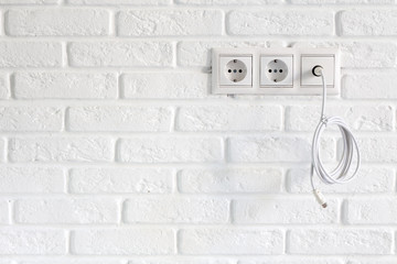 Row of power and tv sockets and tv cable on brick wall