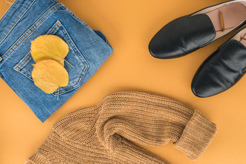 Woman fall/winter clothes laying on yellow background. Jeans, yellow knitted jumper, black flat shoes. Fashion blogger. Minimal concept. 2018 trend. Street style. Stylish. Flat lay.