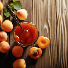 Glass Jar of Apricot jam on wooden table with ripe apricots at background. Top view.