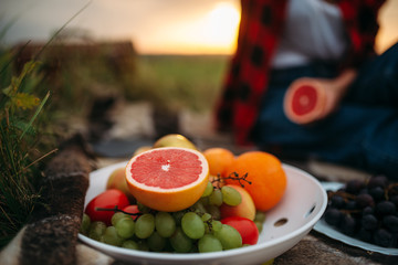 Female person with fruits sitting on plaid, picnic