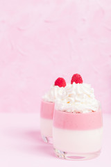 Raspberry panna cotta decorated with cream and ripe berry on pastel pink background.