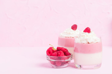 Raspberry panna cotta decorated with cream and ripe berry on pastel pink background.