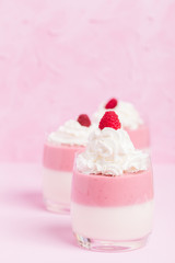 Raspberry panna cotta decorated with cream and ripe berry on pastel pink background.