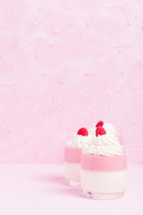 Raspberry panna cotta decorated with cream and ripe berry on pastel pink background.