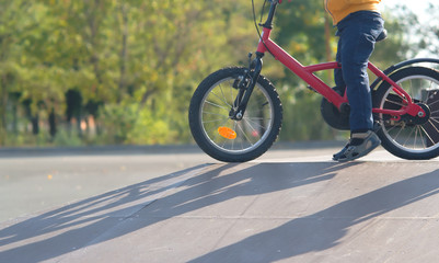 the child skates in a skate park on a bicycle close-up in the rays of the setting sun in the autumn day