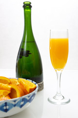Glass of mimosa cocktail ready to be served for brunch with an orange slice with a champagne bottle and a bowl of orange slices on a white table