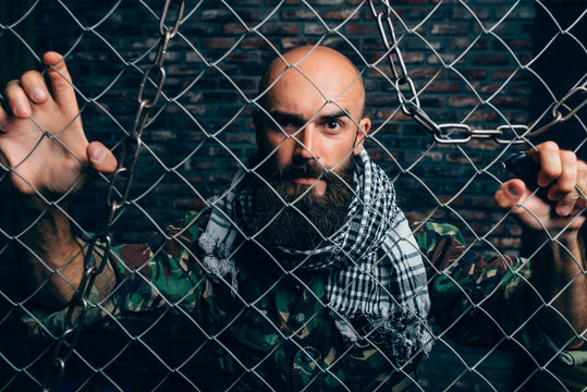 Portrait of man in camouflage standing behind chain link fence