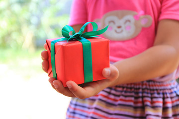 Selective focus of Little girl hands holding gift box with red ribbon for Christmas  and New Year's Day or Greeting season
