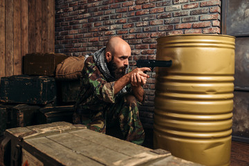 Man in camouflage aiming with gun indoors