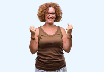 Middle age hispanic woman wearing glasses over isolated background celebrating surprised and amazed for success with arms raised and open eyes. Winner concept.