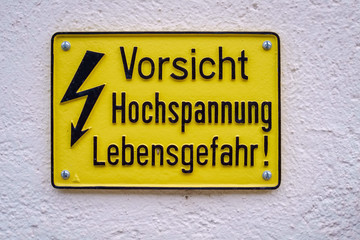 Fototapeta premium Yellow warning sign against a white wall that alarms us for the possible danger of a high voltage (Switzerland)