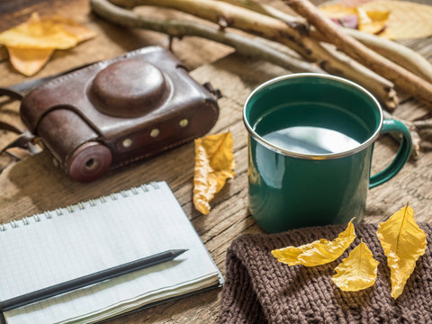 Autumn still-life. Enameled mug, old camera, Notepad, pencil, bread, autumn yellow leaves, dry branches on wooden background