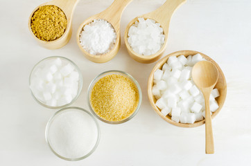 Different kinds of sugar in glass and wooden bowl on white wooden table