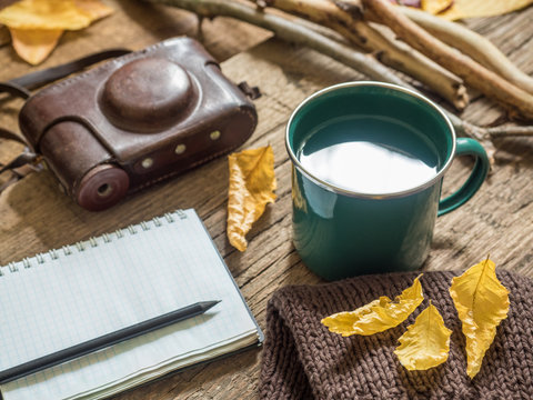 Autumn still-life. Enameled mug, old camera, Notepad, pencil, bread, autumn yellow leaves, dry branches on wooden background