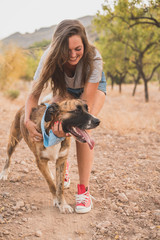 Happy young woman hugging and having fun with her dog with a blue handkerchief around his neck...