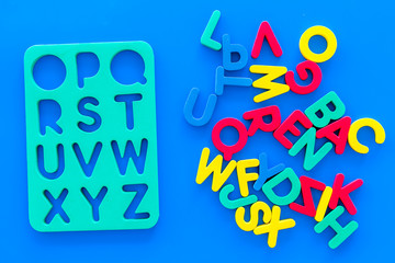 Alphabet for kids concept. English letters in disorder near stencil on blue background top view