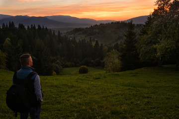 Naklejka na ściany i meble A traveler-photographer observes the sunset over the forest and mountains in the Ukrainian Carpathians