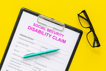 Social security. Disability claim form near pen and glasses on yellow background top view