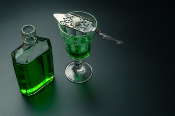 an absinthe bottle, a glass of absinthe and a stainless steel slotted spoon with the sugar cube on the table