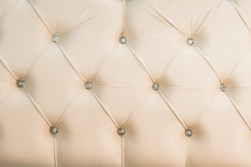 Beige soft textile background with symmetrical buttons on the corners of diamonds. Soft and expensive furniture elements. Luxury background